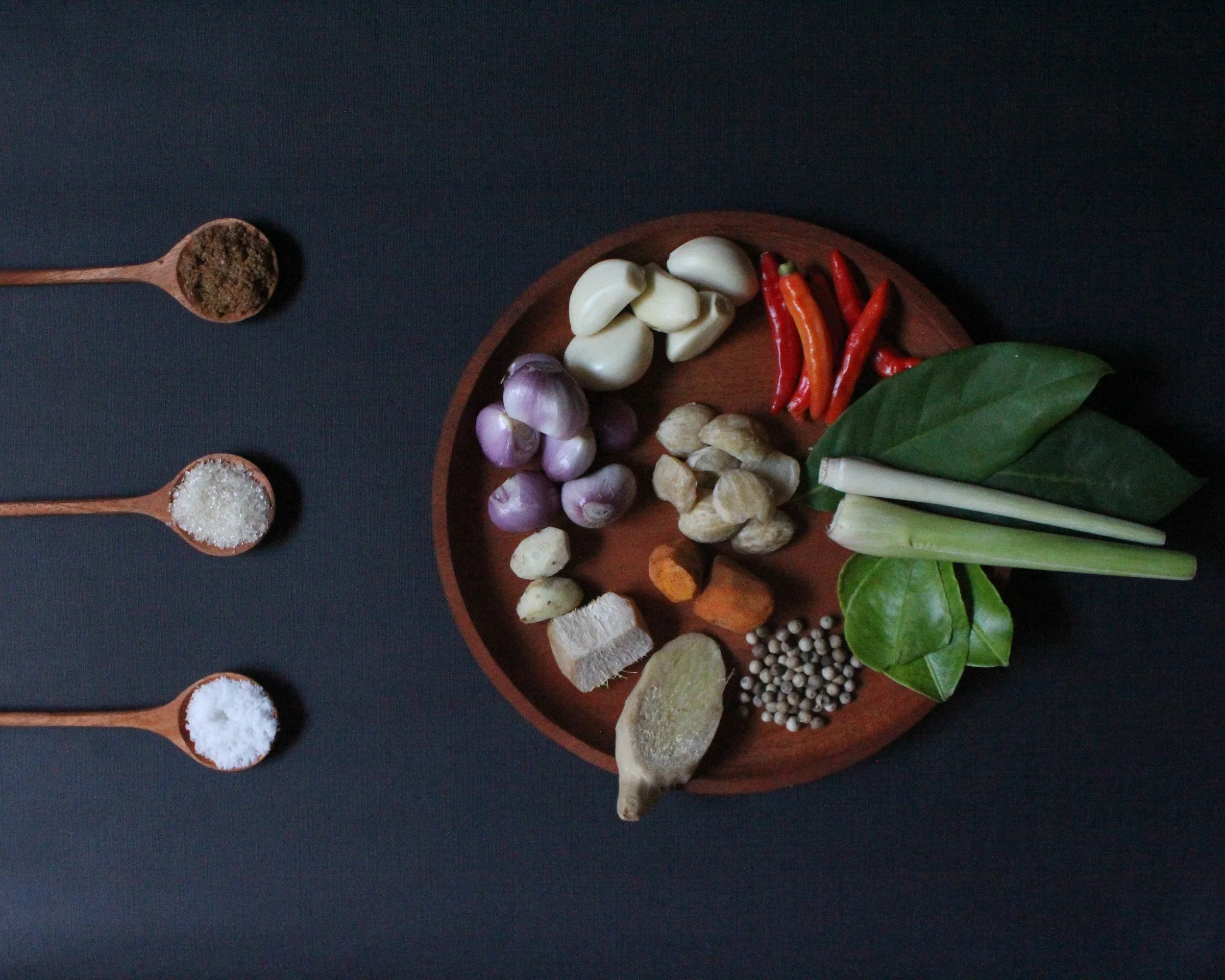 The raw spices for Balinese betutu paste: shallots, garlic, galangal, turmeric, lemongrass, chillies and candlenuts on a wooden plate