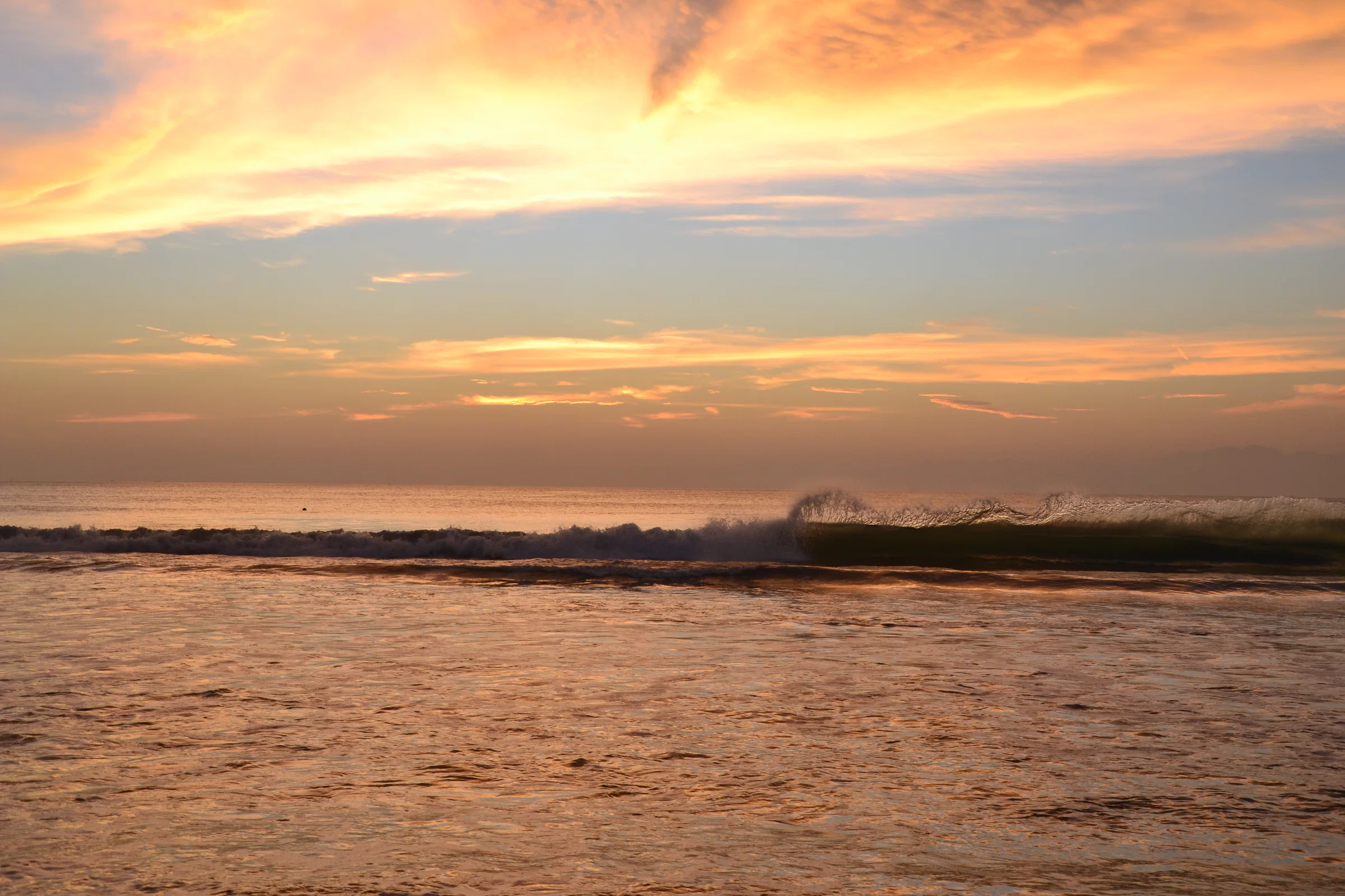 An orange sunset over the breaking waves of Jimbaran Bay