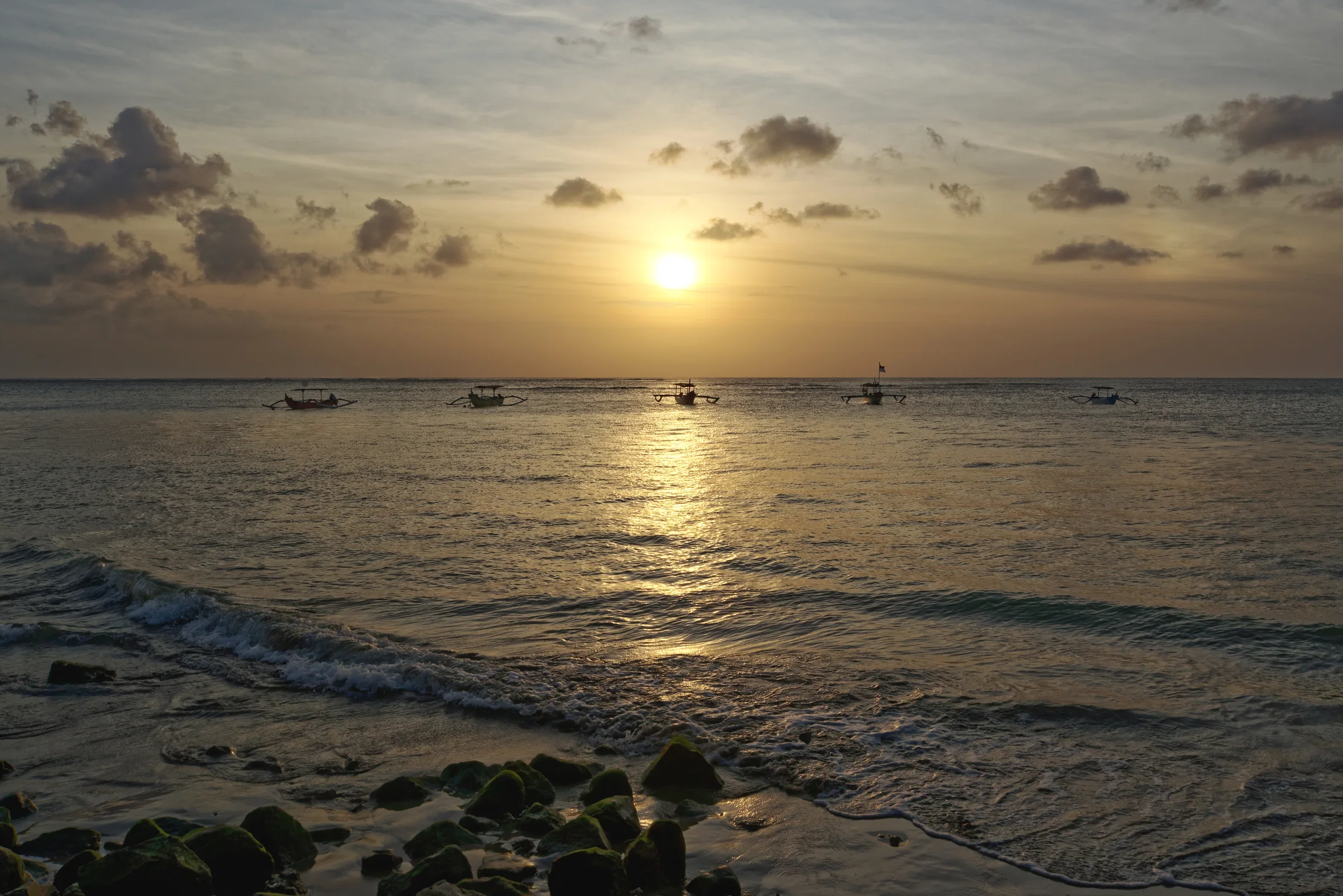The sun setting over the sea at Kuta Beach, with small boats on the horizon