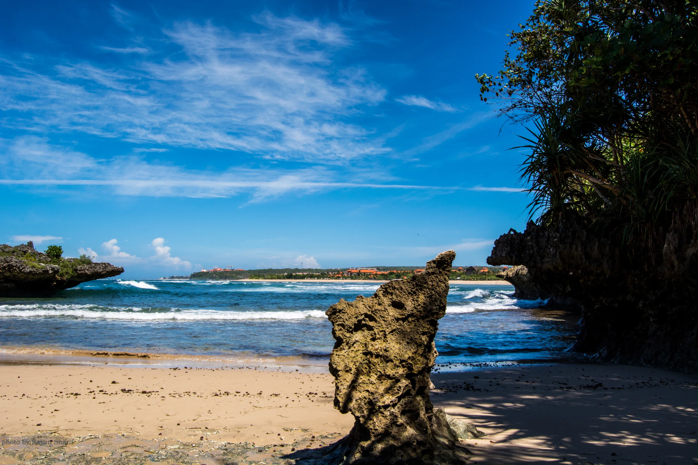 Golden sand, a weathered rock and blue water on a beach of the Nusa Dua peninsula