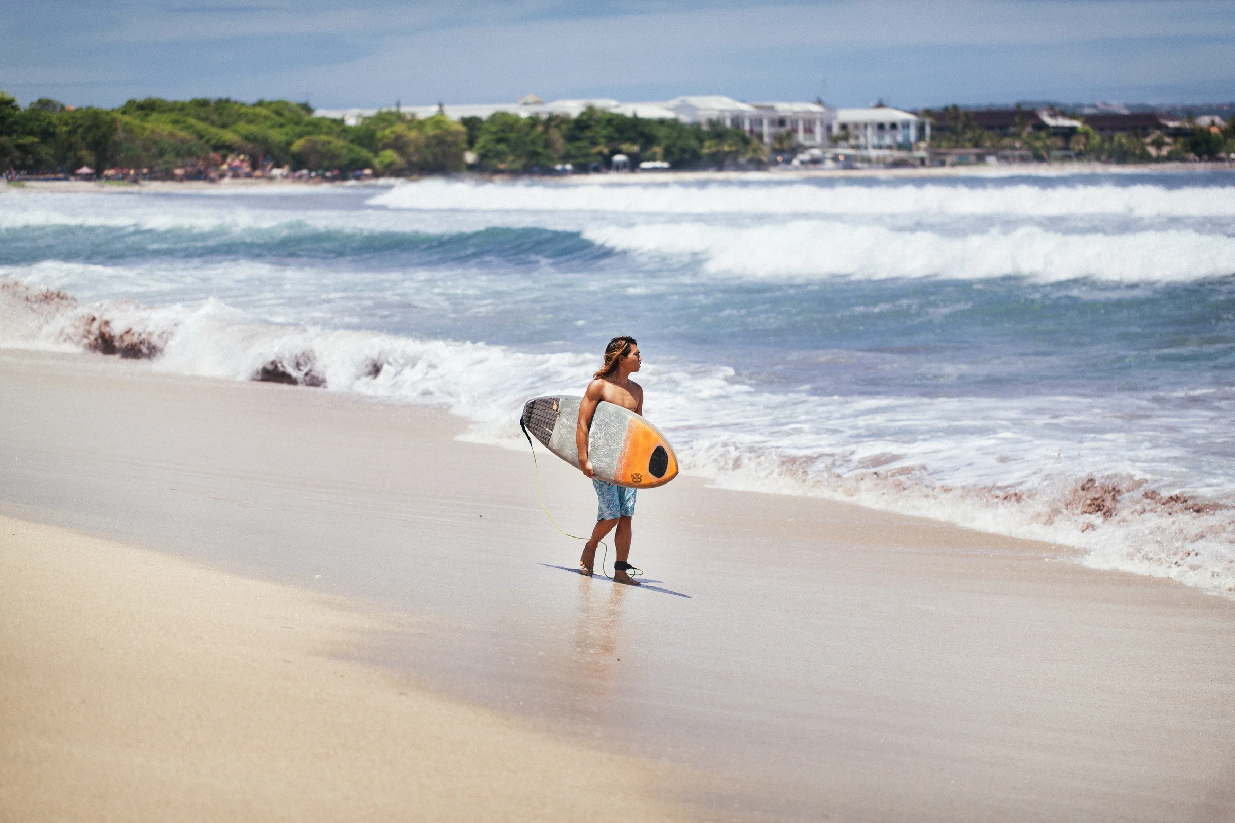A surfer walking along Kuta Beach with a board under the arm