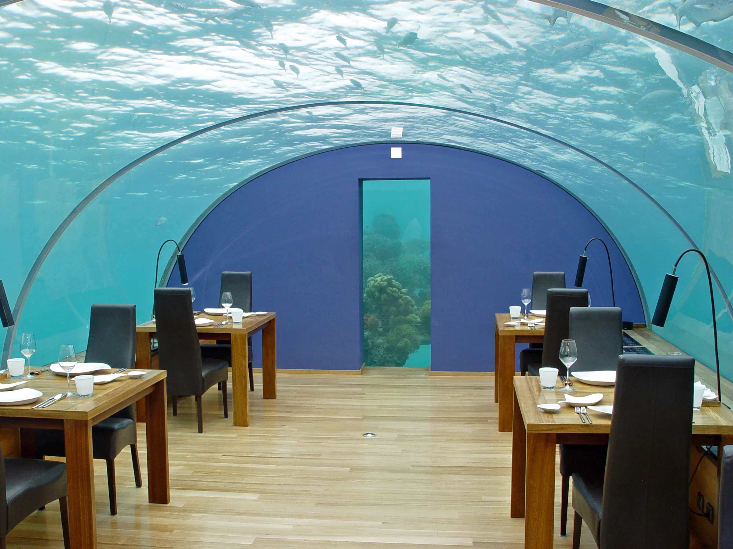 Inside Ithaa, laid tables beneath a curved acrylic roof with the sea above