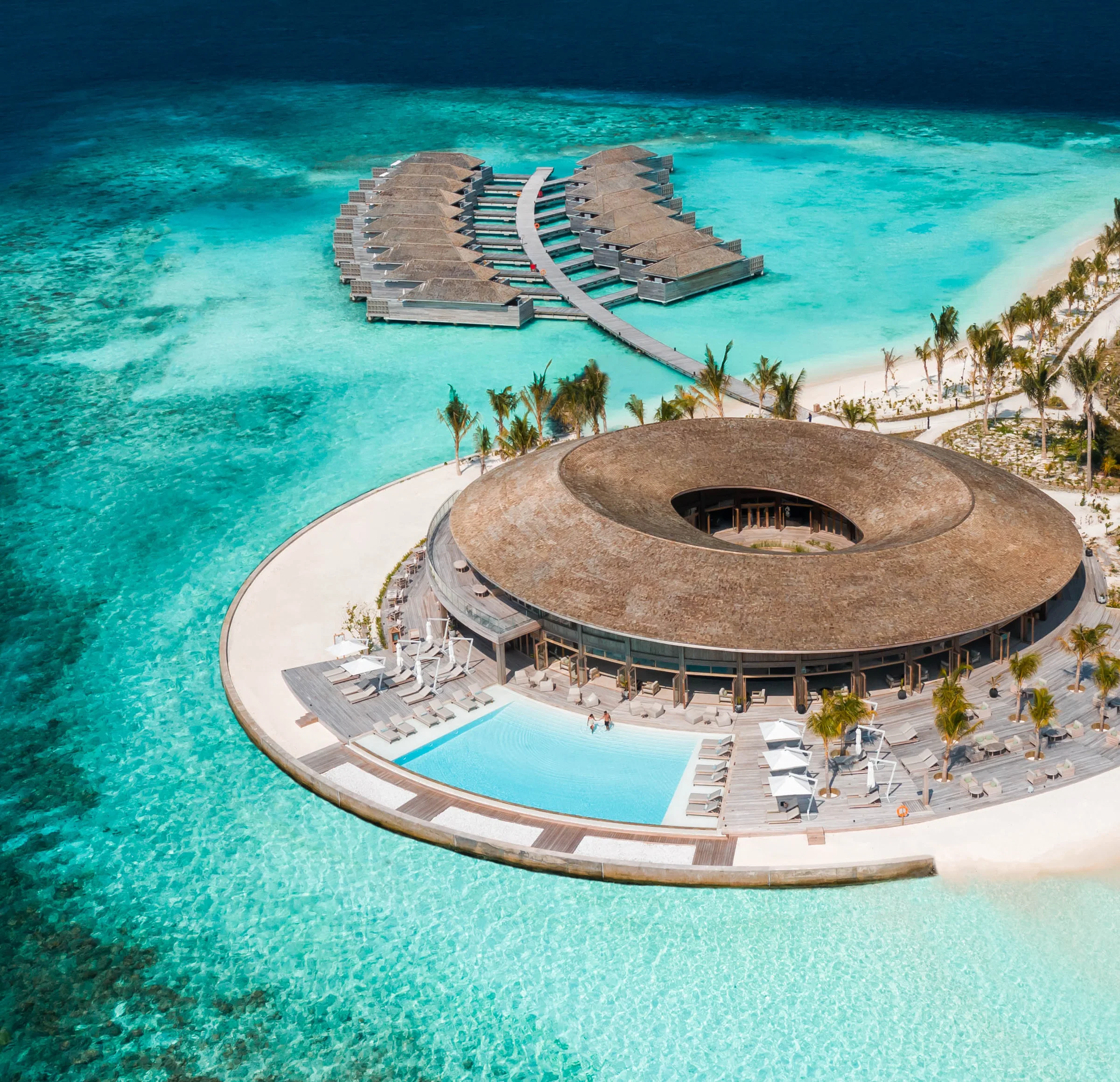 Aerial view of a spa island with a circular thatched pavilion, overwater rooms and a pool, North Malé Atoll