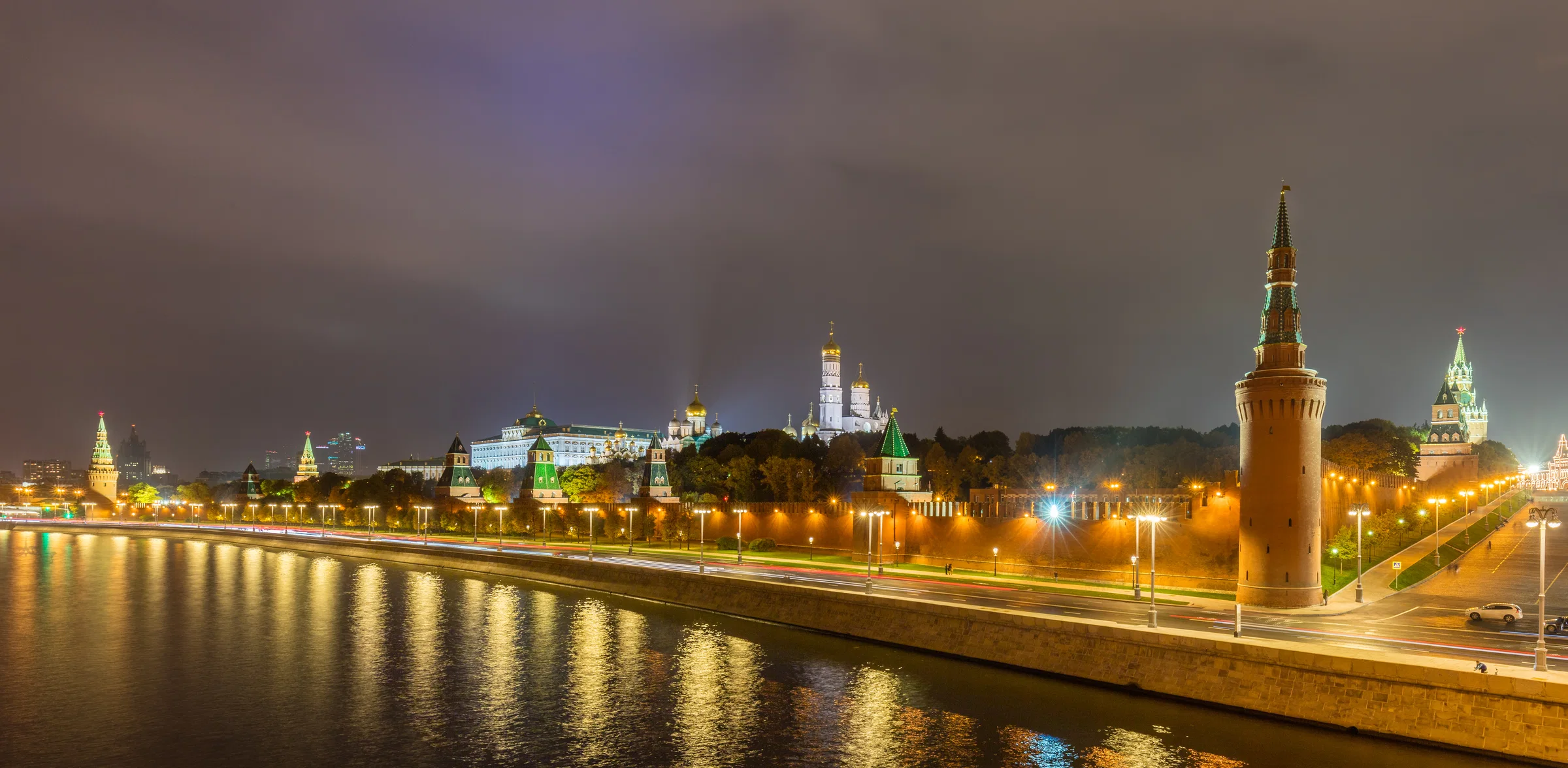 The Moscow Kremlin at night, its walls and towers lit above the Moskva River embankment