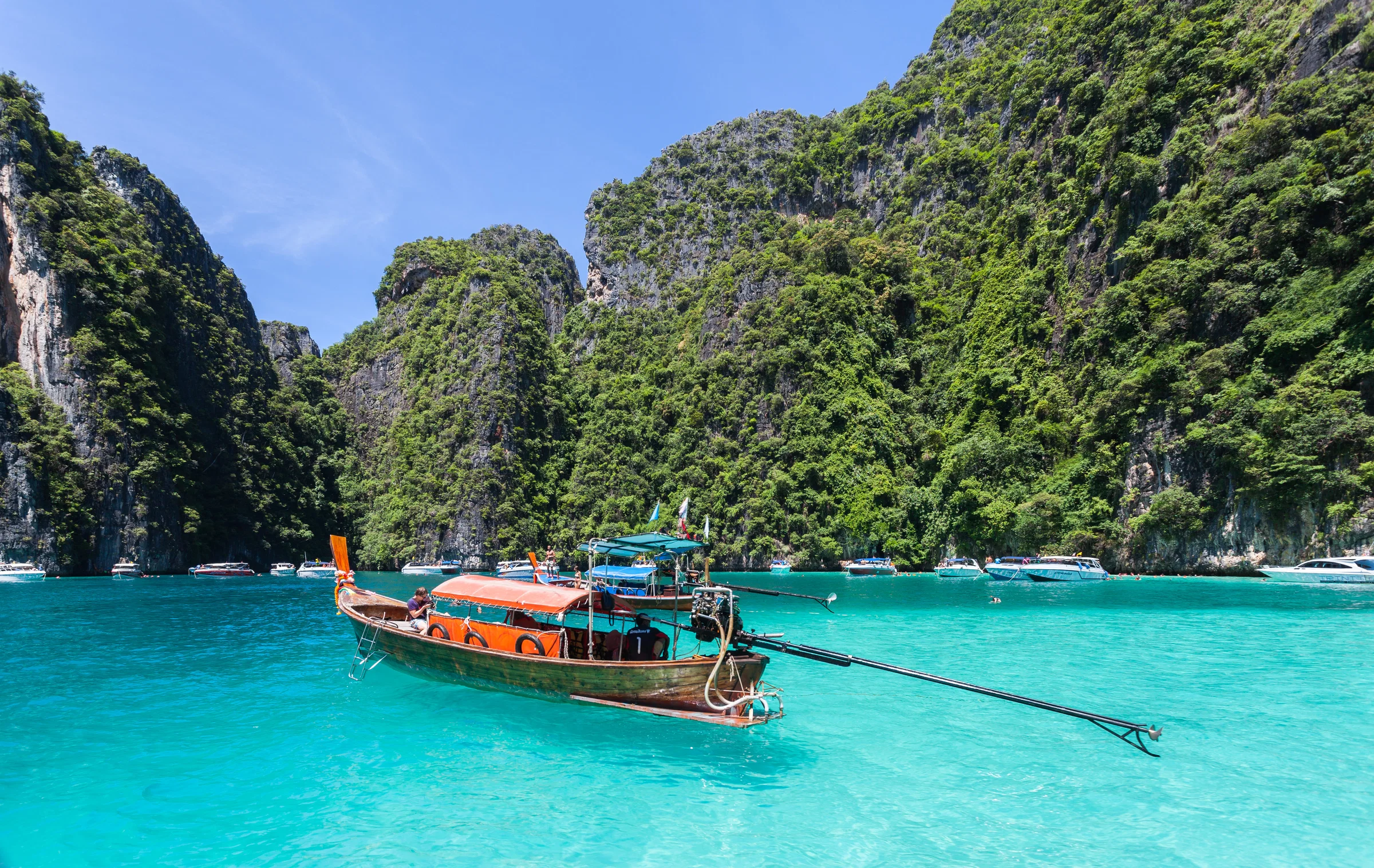 Long-tail boat in the turquoise water below the limestone cliffs of Ko Phi Phi Le