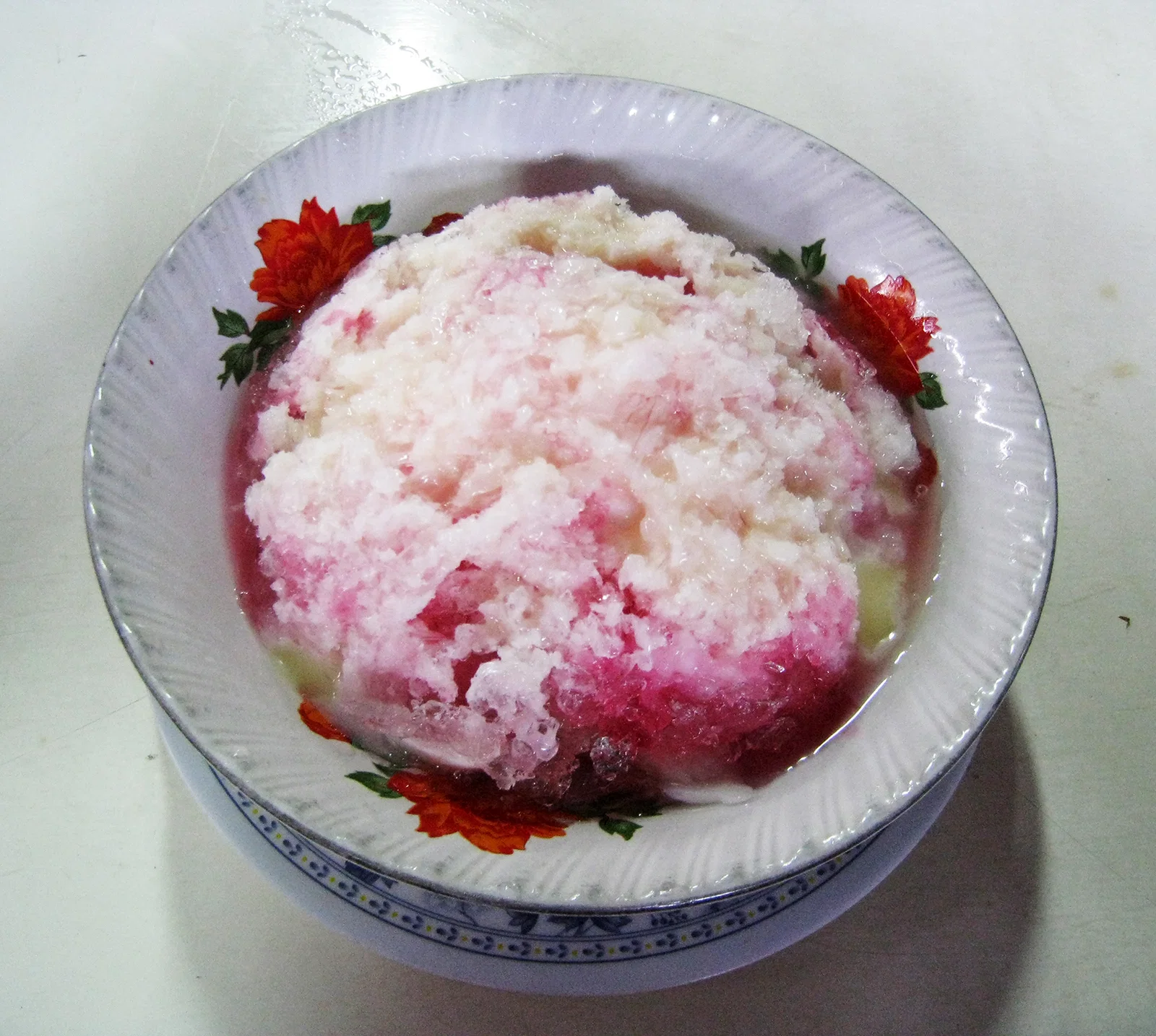 A bowl of es campur, shaved ice with pink syrup and condensed milk