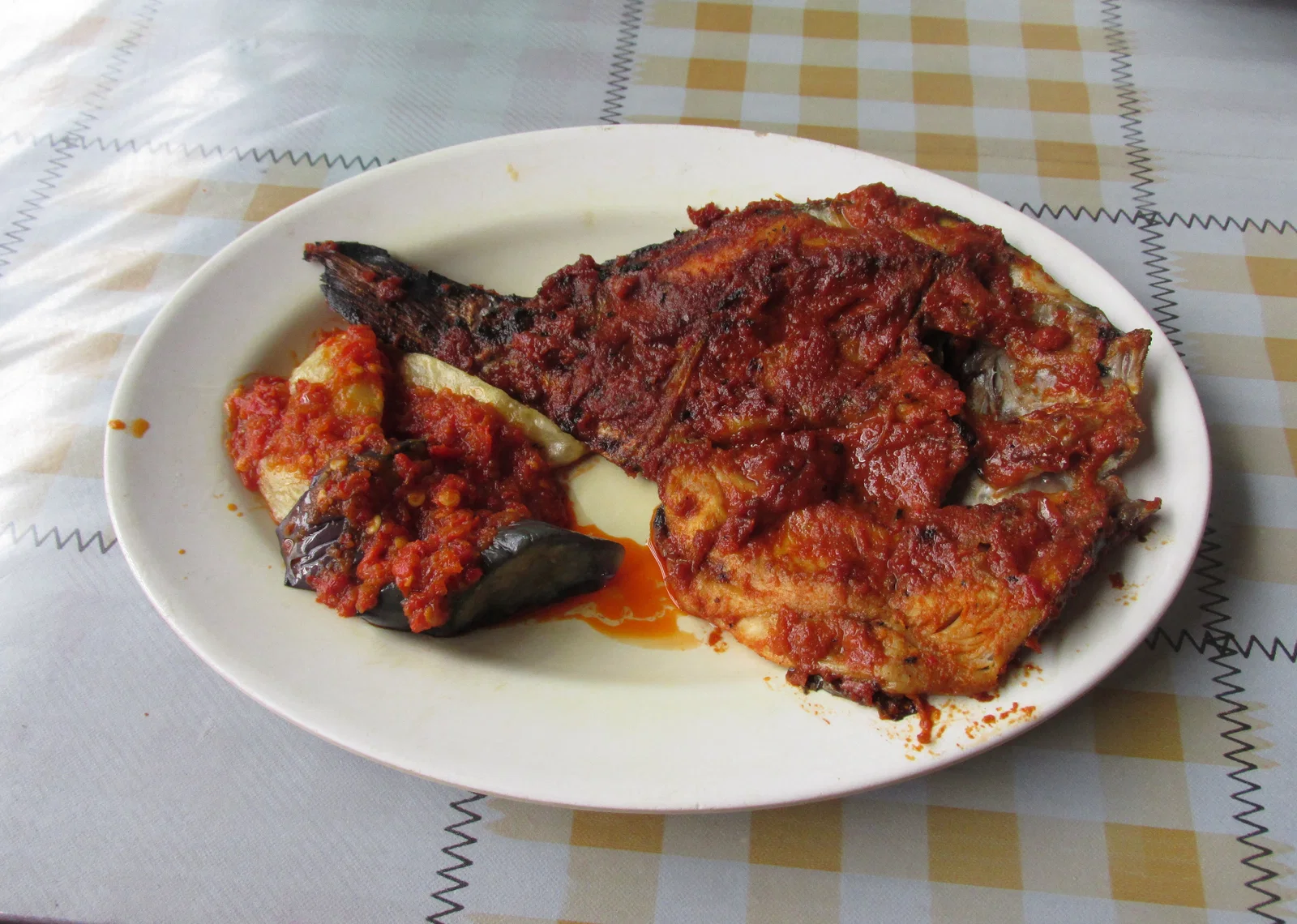A grilled fish glazed with red spice paste on a white plate
