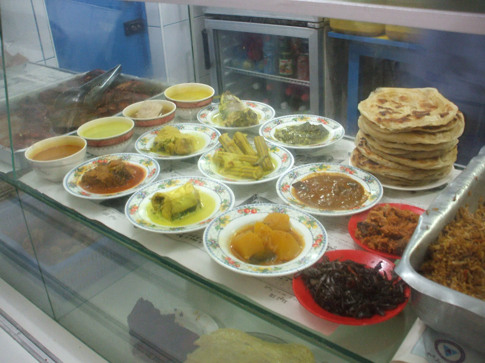 A café counter in Malé with curries, short eats and stacks of roshi