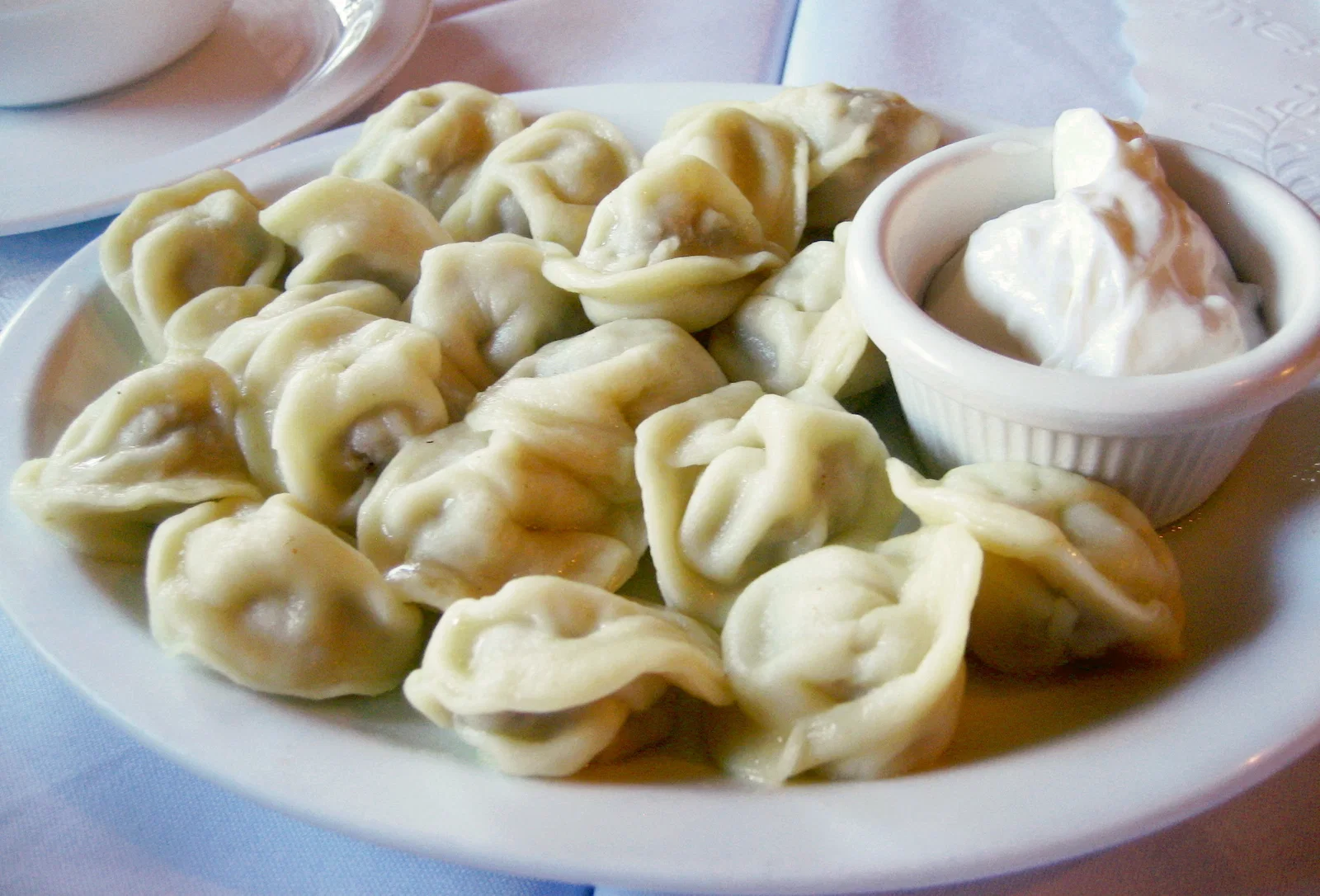A plate of boiled pelmeni with a dish of sour cream