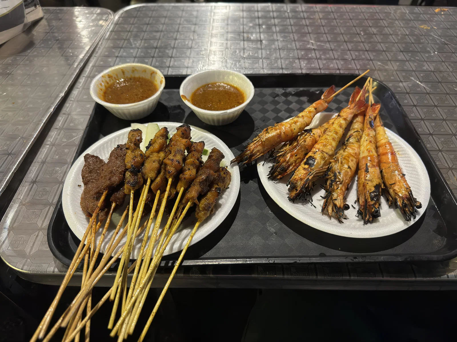 Plates of grilled satay skewers and prawns with bowls of peanut sauce at Lau Pa Sat