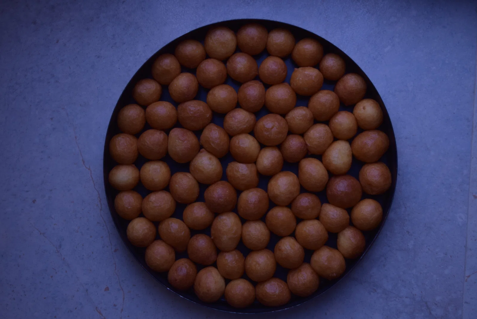 A round tray of golden luqaimat before the syrup is poured