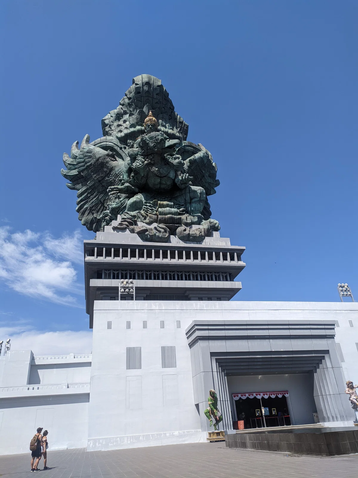 The Garuda Wisnu Kencana statue on its white pedestal against a blue sky