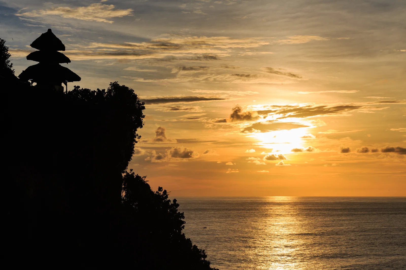 The silhouette of Pura Luhur Uluwatu on its cliff against a golden sunset over the sea