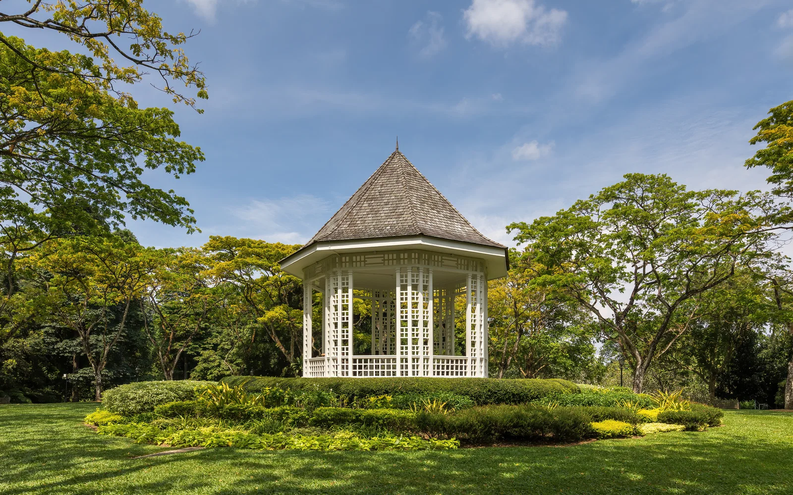 The white bandstand among lawns and tall trees in the Singapore Botanic Gardens on a sunny afternoon
