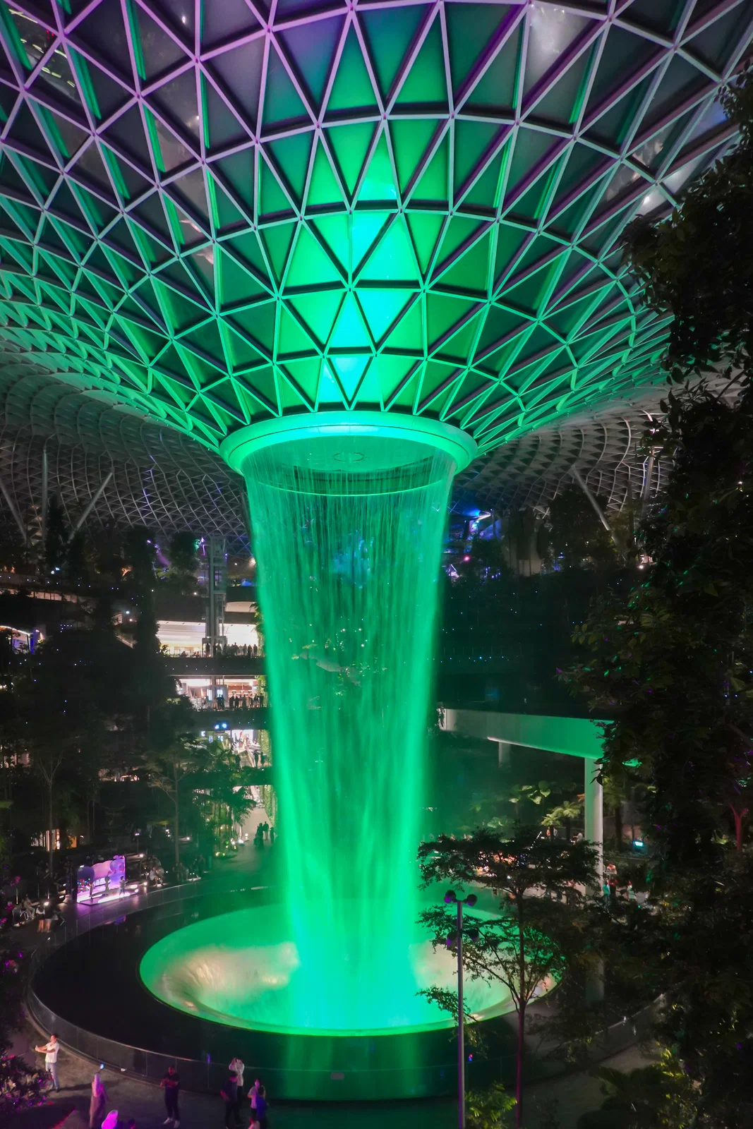 The Rain Vortex lit green at night inside Jewel Changi Airport
