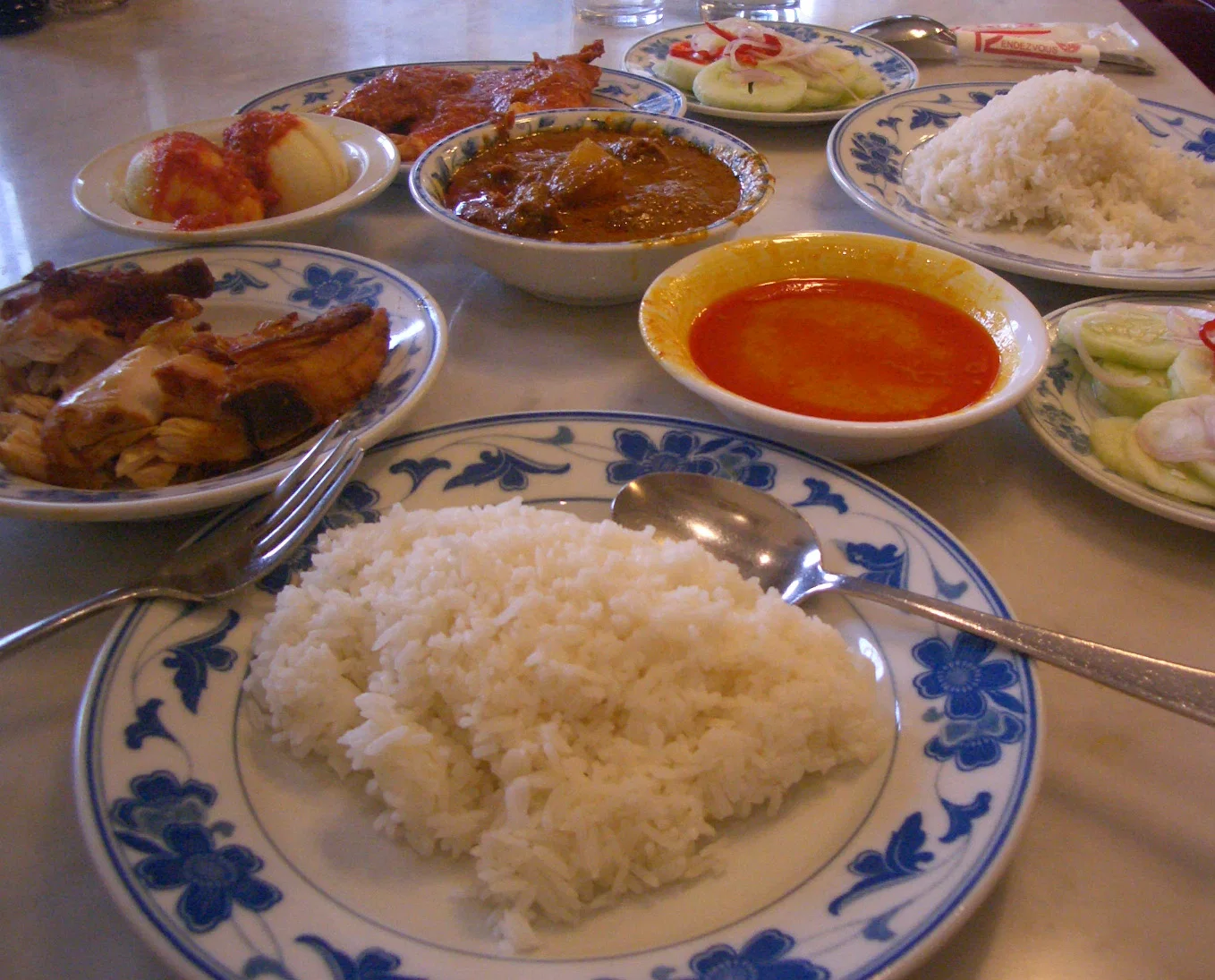A table of nasi padang in Singapore: plates of rice with curries, sambal and side dishes