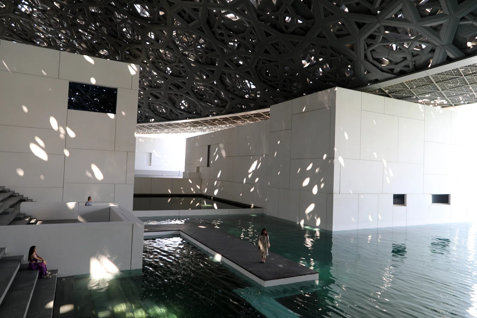 White galleries and water beneath the latticed dome of Louvre Abu Dhabi